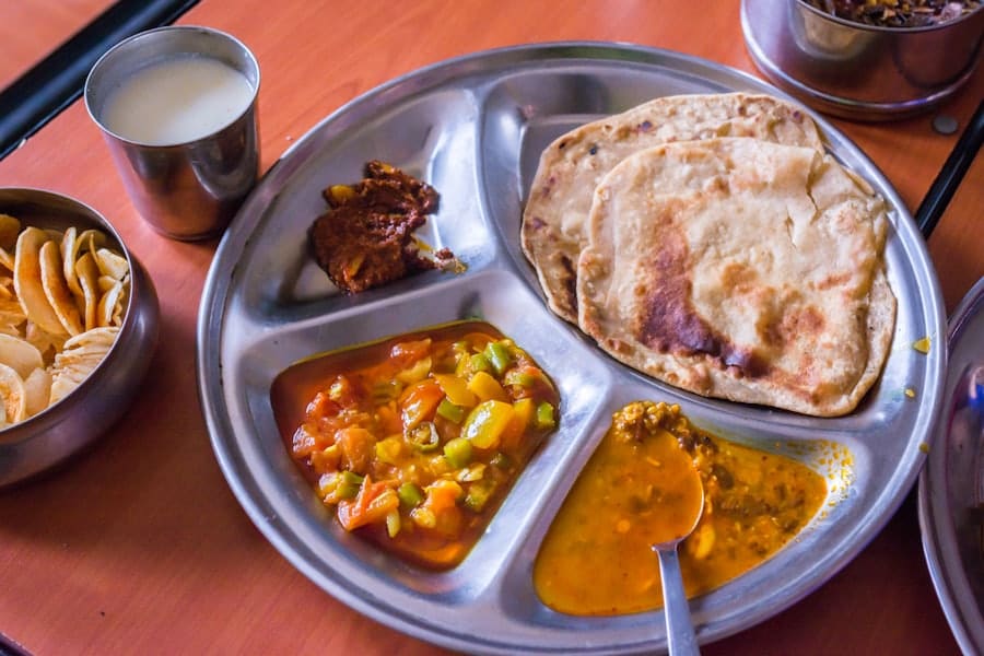 A steel thali of roti, dal and sabzi with a glass of lassi